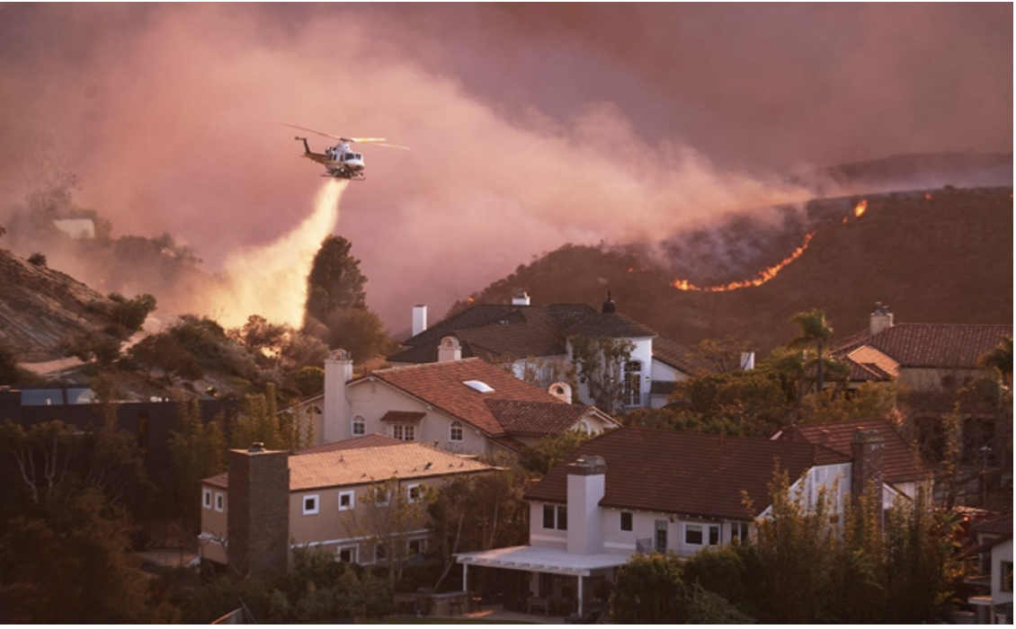 “A helicopter drops water around homes threatened by the wind-driven Palisades Fire in Pacific Palisades". as stated in Teen Vogue.

